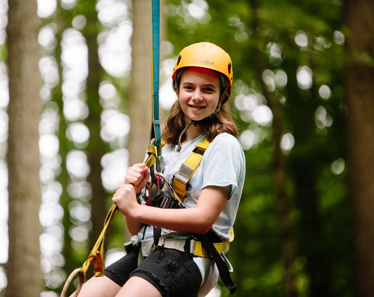 A young girl ziplines through the trees at Camp Kesher